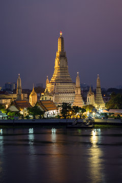 Beautiful view of lit Wat Arun temple next to Chao Phraya River in Bangkok, Thailand, at dusk.