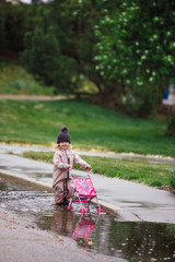 Fototapeta na wymiar Little girl playing with toy stroller in puddles