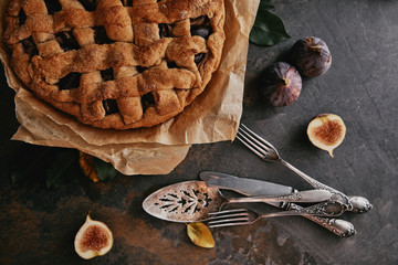 flat lay with homemade pie on baking paper, antique cutlery and fresh figs on dark tabletop