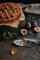 close up view of homemade pie on baking paper, antique cutlery and fresh figs on dark tabletop