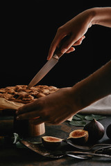 cropped shot of woman cutting pie on baking paper with knife on surface with figs