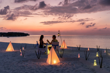 Romantisches Paar sitzt bei einem privatem Abendessen am tropischen Strand und genießt den...