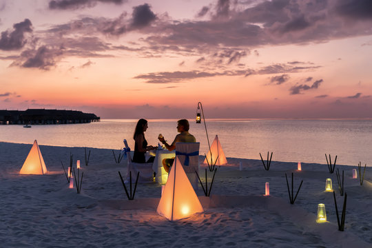 Romantisches Paar sitzt bei einem privatem Abendessen am tropischen Strand und genie&szlig;t den Sonnenuntergang