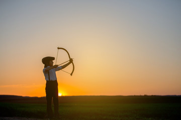 Silhouette of child playing with bow and arrows, archery shoots a bow at the target.