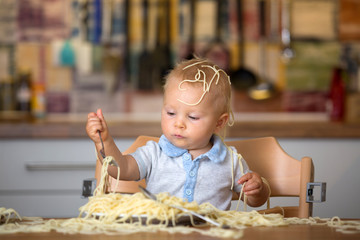 Little baby boy, toddler child, eating spaghetti for lunch and making a mess