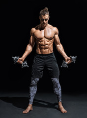 Fototapeta na wymiar Athletic man working out with dumbbells. Photo of handsome man with good physique on black background. Strength and motivation. Full length