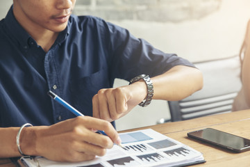 Time out concept.Business man seeing wrist watch to check time at office.Boss look at clock to work.On Wooden desk with calendar,laptop,annual and summary report.It's Time out for appointment meeting.