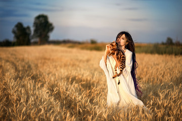 sunset photo shoot of a girl with dreadlocks in a white dress in wheat with a Bengal cat