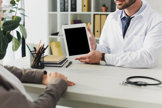 cropped image of doctor showing tablet with blank screen to patient in clinic