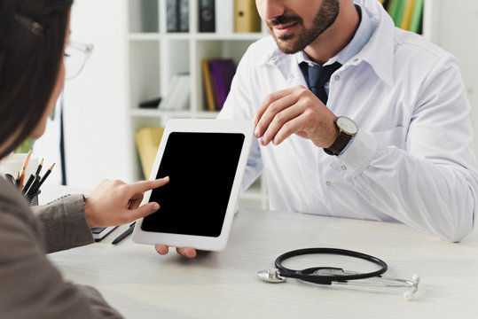 cropped image of doctor showing patient tablet with blank screen in clinic