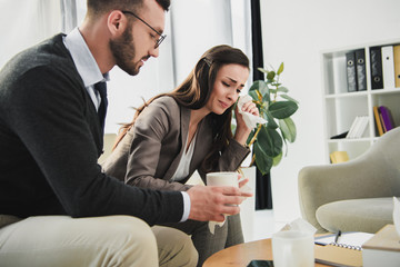 psychologist giving cup of tea to crying patient in doctors office