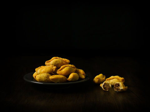 Packshot close up view of "Pan Klib" traditional mini Thai puff dessert stuffed material with fish, curry, shallot, pepper seasoned sugar and salt in black plate on black background with copy space