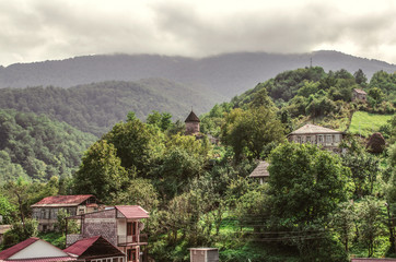 Fototapeta na wymiar Chapel of St. Sarkis and houses in the mountain village of gosh with a darkened sky of thick fog, located in the forest, near the town of Dilijan 