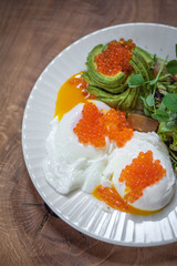 Delicious breakfast with poached eggs, red caviar and sliced avocado