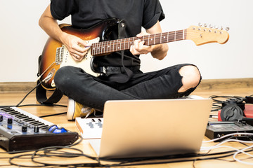 Male guitarist playing electric guitar at modern home studio or rehearsal room. Young man producing...