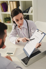 Fototapeta premium female doctor showing insurance claim form to man in office