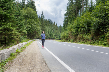 Young smiling woman jogging on mountain road. Happy girl with long hair running in mountains in autumn. Healthy lifestyle background with copy space