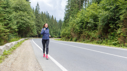 Obraz premium Young smiling woman jogging on mountain road. Happy girl with long hair running in mountains in autumn. Healthy lifestyle background with copy space