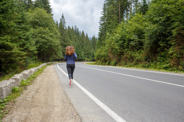 Running girl on the road. Young slim woman jogging in mountains. Rear view with copy space