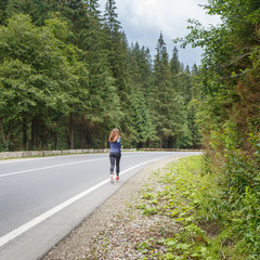 Running girl on the road. Young slim woman jogging in mountains. Rear view with copy space