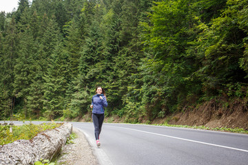 Obraz premium Young smiling woman jogging on mountain road. Happy girl with long hair running in mountains in autumn. Healthy lifestyle background with copy space