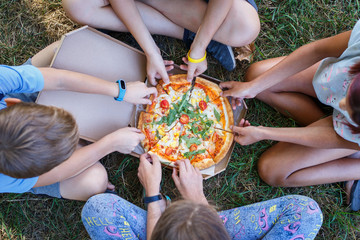 Top view image of children grab slices of pizza from box at the outdoors picnic. Children hands...