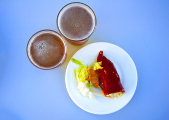 Red stuffed paper with salad and sauce on white plate and two beers