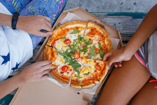 Two girls eating pizza outdoors together. Top view image of summer picninc concept
