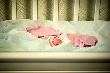 pink baby's dummy, cap and socks in a cot