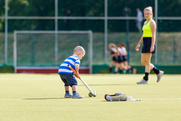 Small boy training playing field hockey with stick on the field