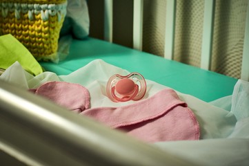 pink baby's dummy, cap and socks in a cot