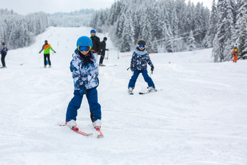 Cute preschool children, skiing in Austrian winter resort on a clear day, wintertime