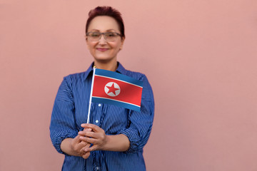 North Korea  flag. Woman holding North Korea flag. Nice portrait of middle aged lady 40 50 years old with a national flag over pink wall background outdoors.