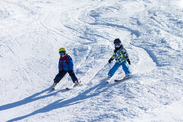 Two young children, siblings brothers, skiing in Austrian mountains on a sunny day