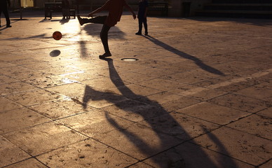 Shadows of people playing in football in a street of the city at the sunset - 220226514