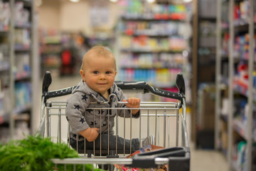 Toddler baby boy, sitting in a shopping cart in grocery store, smiling and eating bread