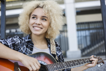 Happy African-American girl playing the guitar the street