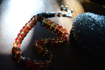 Muslim religious beads, tesbih of yellow and red beads with a metal sponge on a lacquered wooden table lit by the rays of the sun