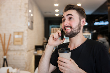 A man communicates on the phone in a cafe and holds coffee in his hand