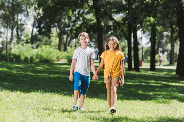 Obraz premium piękne uśmiechnięte dzieci, trzymając się za ręce i spacerując razem w parku