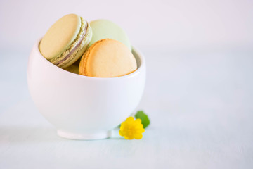 Macarons in white porcelain bowl on blue wooden table with nice yellow flower