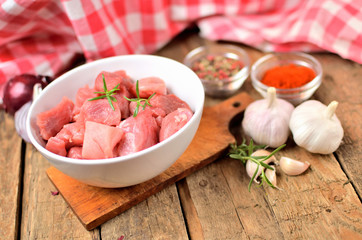 Raw pork meal diced in a bowl, garlic, half of onion, sweet pepper and checkered red tablecloth in the background