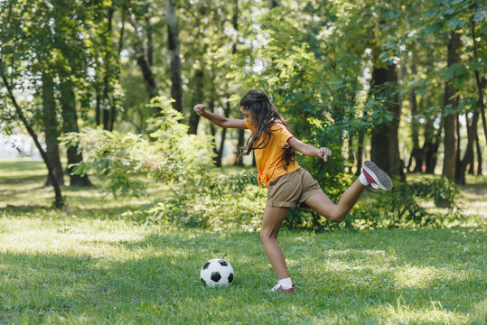 side view of child kicking soccer ball in park