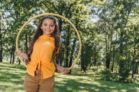 beautiful happy kid holding hula hoop and smiling at camera in park