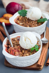 Plum crumble pie or plum crisp with oats and spices, served with vanilla ice cream ball, in baking dish, vertical