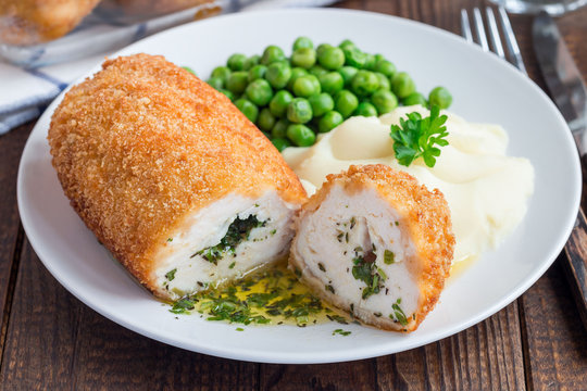 Chicken Kiev, ukrainian cuisine. Cutted chicken cutlet in bread crumbs stuffed with butter and herbs, served with mashed potato and green peas, on brown background, horizontal, closeup