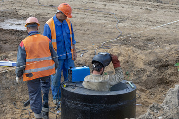 Workers at the construction site welding stairs in the sewage well