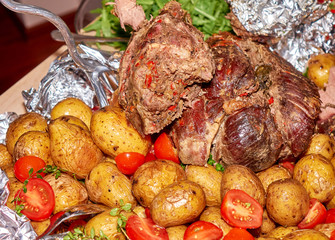Big peace of the roasted mutton meat with baked potatoes and fresh tomatoes