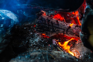 Smoldered logs burned in vivid fire. Atmospheric background with orange flame of campfire. Unimaginable detailed image of bonfire from inside with copy space. Smoke and ashes close up.