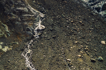 Detailed natural texture of slope from loose stones. Mountain water stream flows down mountainside. Small waterfall on rock. Unusual landscape of majestic nature.